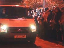 A large crowd is silent as the bodies of the family are removed.